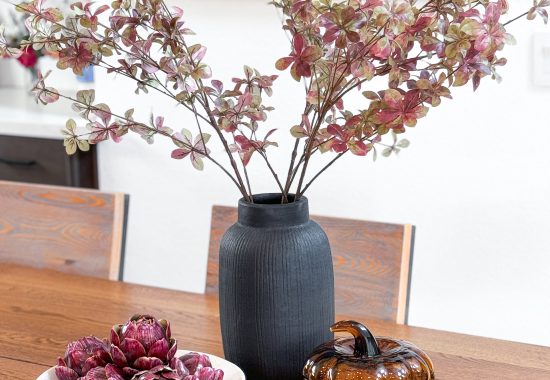 Fall stems in a black vase sitting on a dining table next to glass pumpkin decor